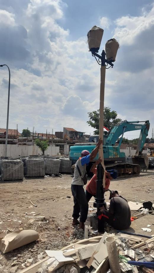 Tiga pekerja mendirikan tiang lampu ornamen dua kepala