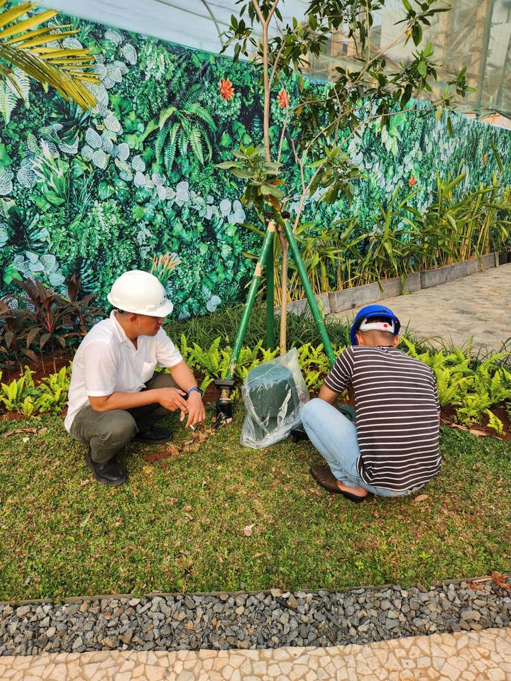 Dua teknisi memasang garden speaker di antara tanaman taman kawasan