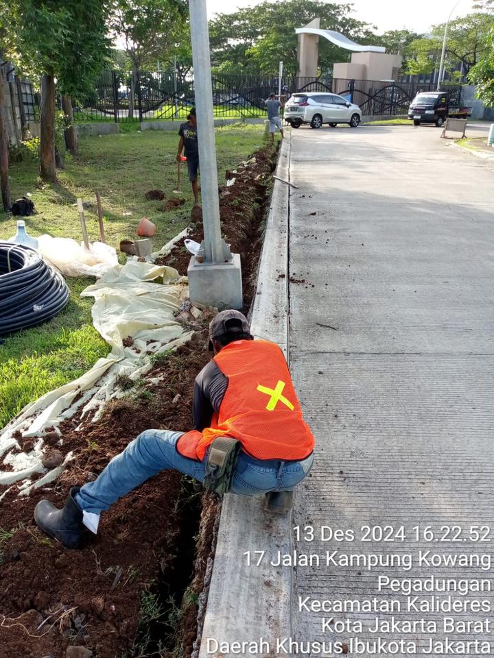 Pekerja menggali jalur kabel di sisi jalan, pipa HDPE hitam menunggu di tepi