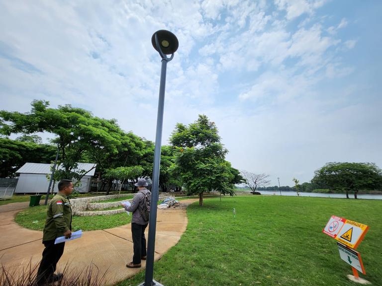 Dua petugas memeriksa tiang lampu taman di tepi danau kawasan